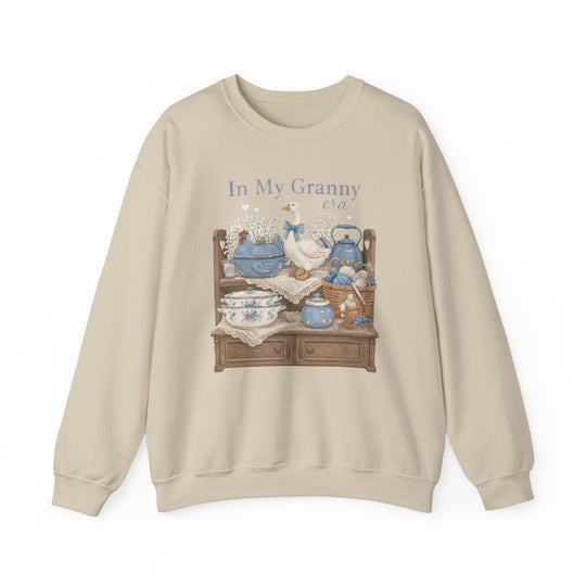 Light-beige In My Granny Era crewneck sweatshirt with vintage-style print featuring a sideboard, ceramic goose, floral teapot set, yarn basket, and baby’s-breath flowers.