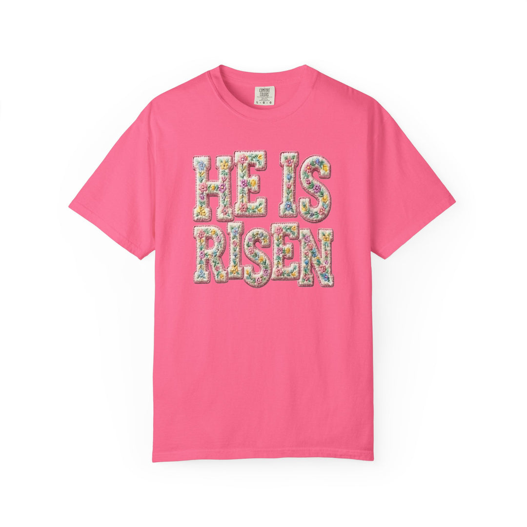 Pink crew-neck T-shirt with HE IS RISEN in pastel floral letters, reflecting Faith Family Designs' unique graphic and spiritual themes.