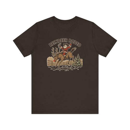 Reindeer Rodeo Tee featuring Santa riding a reindeer in a winter rodeo scene, captures holiday cheer. Soft cotton, unisex fit, perfect for festive occasions.