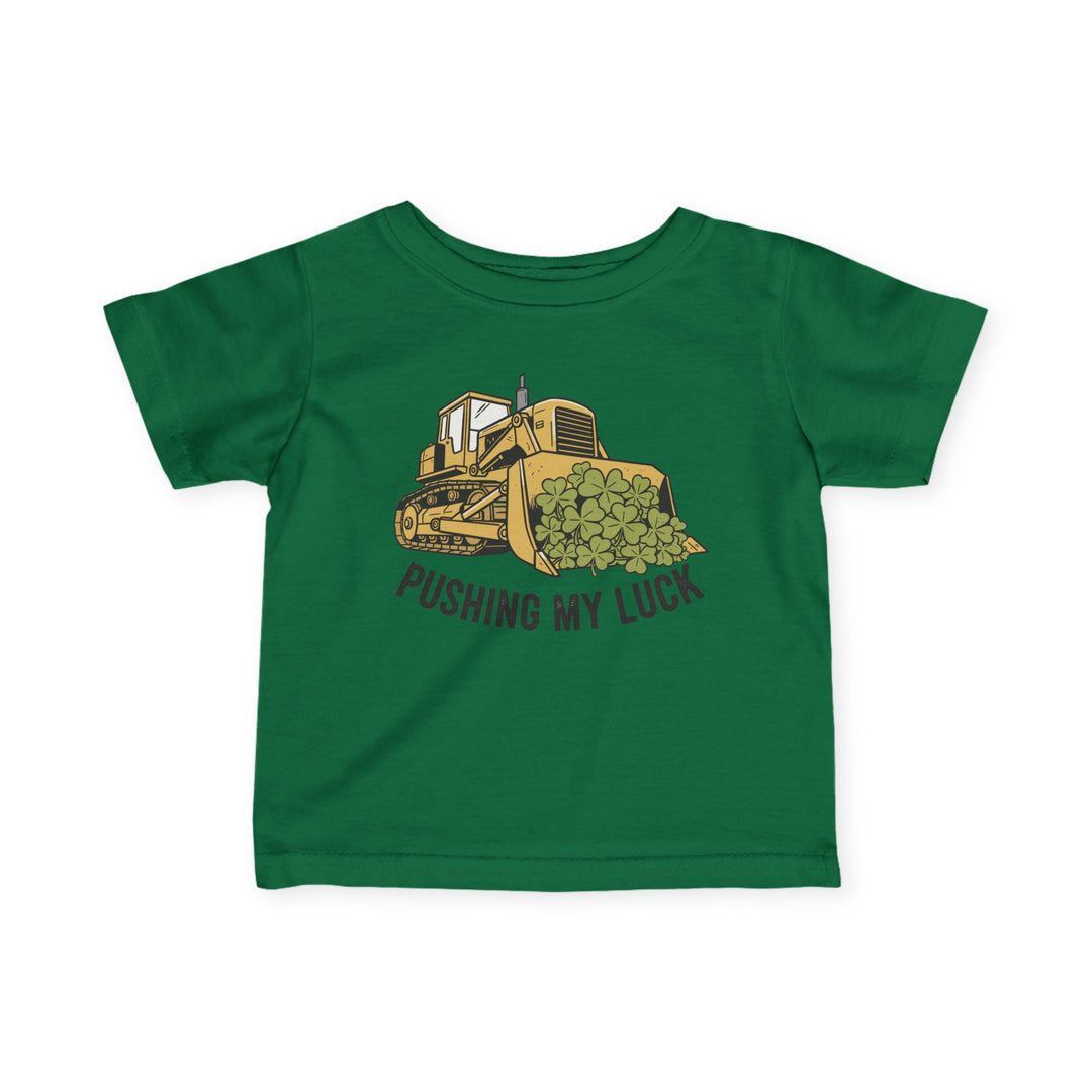 Pushing My Luck Baby Tee: Green infant T-shirt featuring a yellow bulldozer illustration with four-leaf clovers and PUSHING MY LUCK text, designed for comfort and durability.
