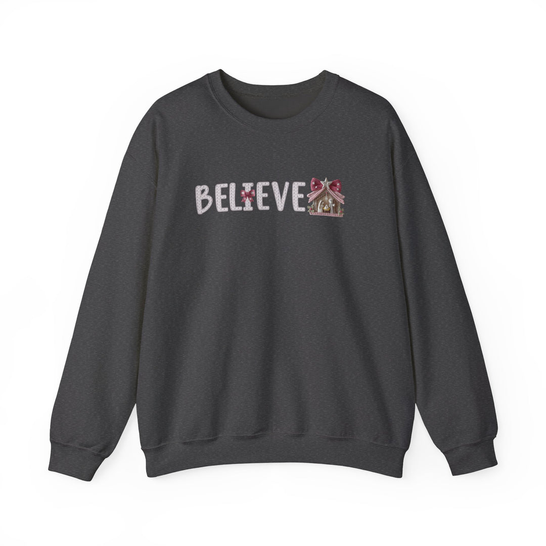 Dark charcoal-gray crewneck sweatshirt featuring BELIEVE in a knitted-look typeface, with a Christmas-themed I and nativity scene replacing the final E.