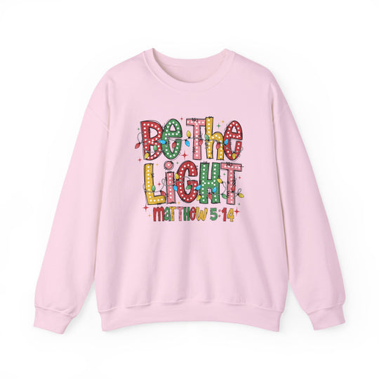 Light-pink crewneck sweatshirt with Be the Light design in Christmas lights style, featuring Matthew 5:14 below. Made from a cotton-polyester blend.