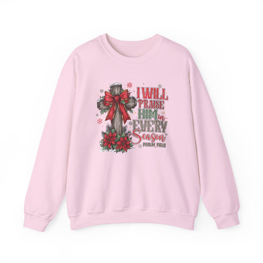 Light-pink crewneck sweatshirt featuring a wooden cross with a red bow, surrounded by evergreens and poinsettias, inscribed with “I WILL PRAISE HIM in EVERY Season,” Psalm 146:2.