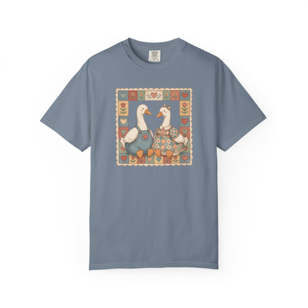 Thrifted Geese Tee: Slate-blue T-shirt featuring two folk-art geese in overalls and dress, framed by stylized hearts. Comfortable, garment-dyed cotton with relaxed fit.