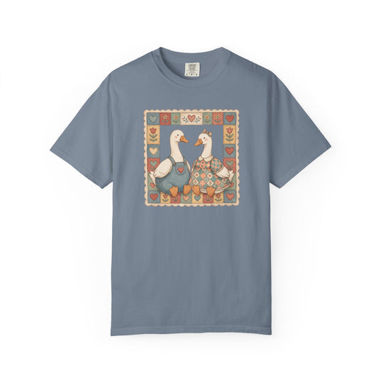 Thrifted Geese Tee: Slate-blue T-shirt featuring two folk-art geese in overalls and dress, framed by stylized hearts. Comfortable, garment-dyed cotton with relaxed fit.