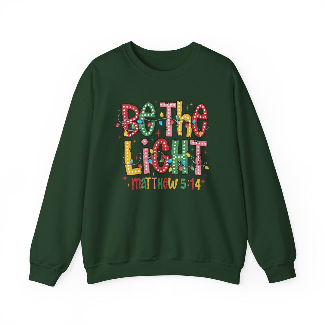 Dark green Be the Light Crew sweatshirt with multicolored festive graphic, featuring Christmas lights and Matthew 5:14 reference, offering comfort and durability.