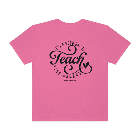 A Teach Tiny Humans Tee, a pink shirt with black text, in a relaxed fit, made of 80% ring-spun cotton and 20% polyester, featuring a rolled-forward shoulder and back neck patch.