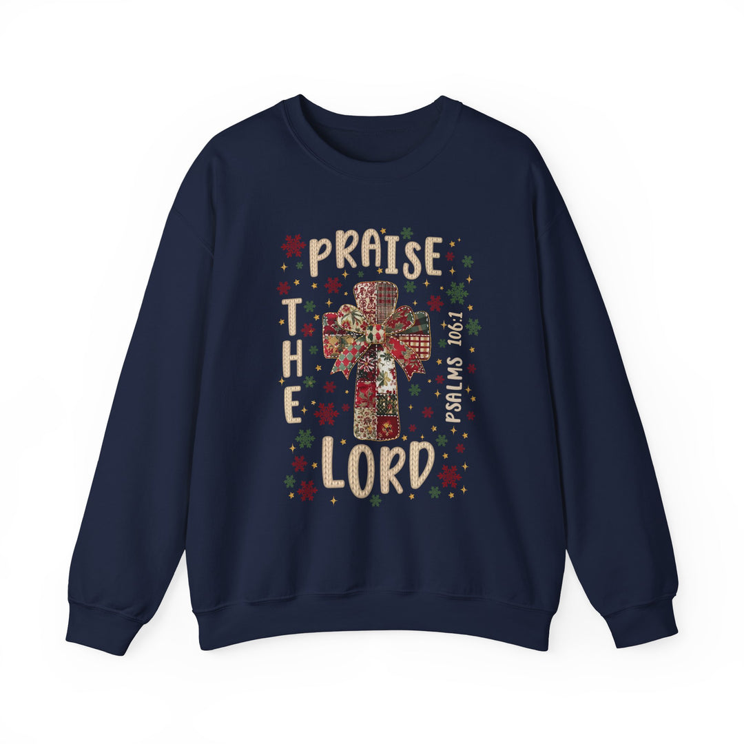 Navy-blue crewneck sweatshirt with patchwork cross and festive bow, surrounded by red and green snowflakes, reads “Praise the Lord” and “Psalms 106:1.”