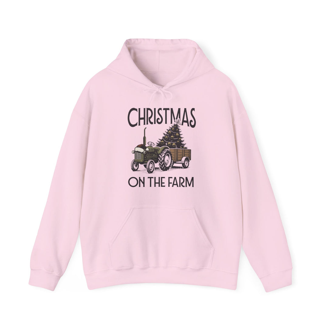 Light-pink hoodie featuring CHRISTMAS ON THE FARM with a tractor and Christmas tree graphic, kangaroo pocket, and drawstrings, ideal for cozy winter wear.