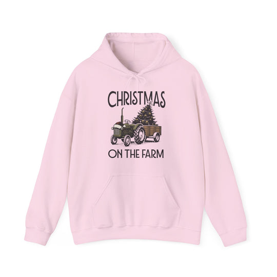 Light-pink hoodie featuring CHRISTMAS ON THE FARM with a tractor and Christmas tree graphic, kangaroo pocket, and drawstrings, ideal for cozy winter wear.