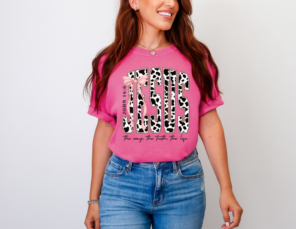 Young woman wearing a John 14:6 Tee with cow-print JESUS design, pink ribbon bow, and biblical reference, accessorized with jewelry.