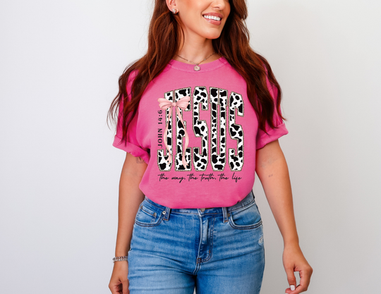Young woman wearing a John 14:6 Tee with cow-print JESUS design, pink ribbon bow, and biblical reference, accessorized with jewelry.