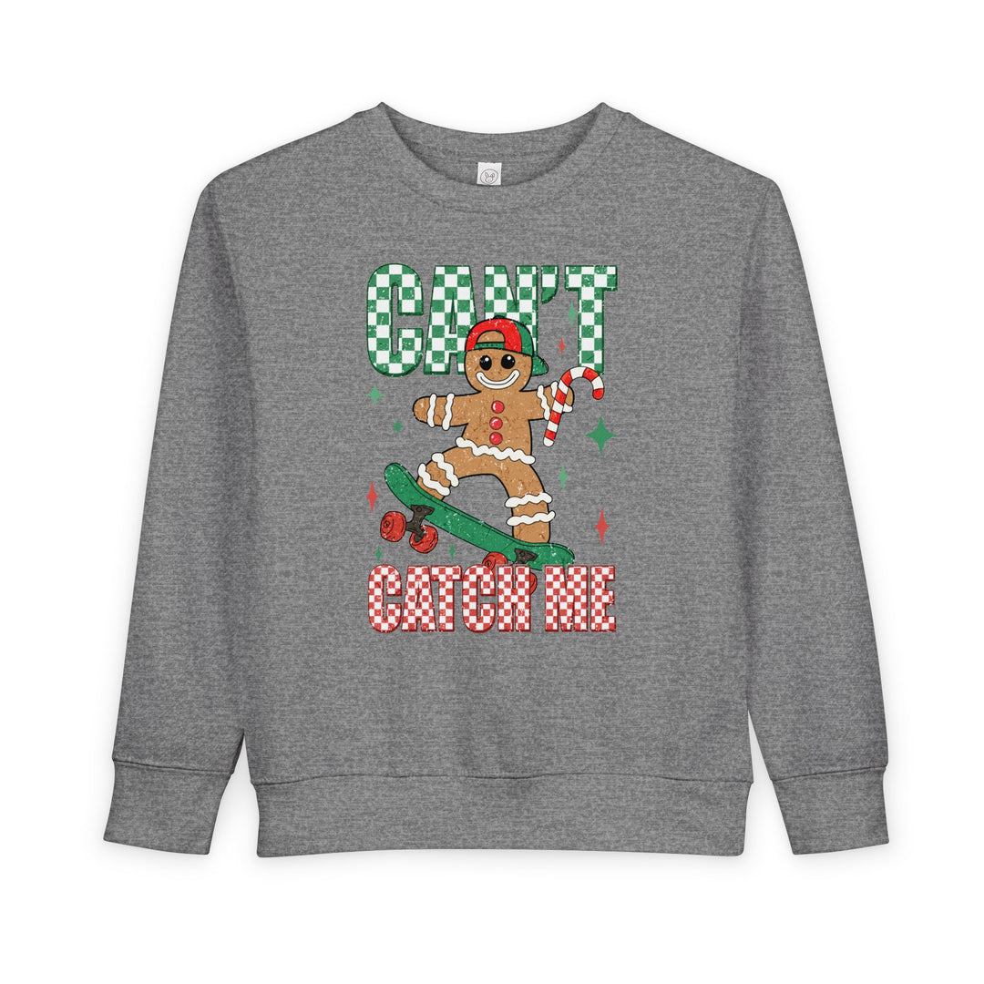 Heather-gray toddler sweatshirt featuring a gingerbread character on a skateboard with CAN'T CATCH ME text, combining festive charm with comfort and durability.