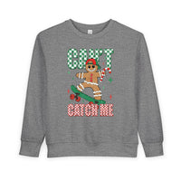 Heather-gray toddler sweatshirt featuring a gingerbread character on a skateboard with CAN'T CATCH ME text, combining festive charm with comfort and durability.