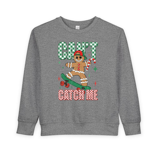 Heather-gray toddler sweatshirt featuring a gingerbread character on a skateboard with CAN'T CATCH ME text, combining festive charm with comfort and durability.
