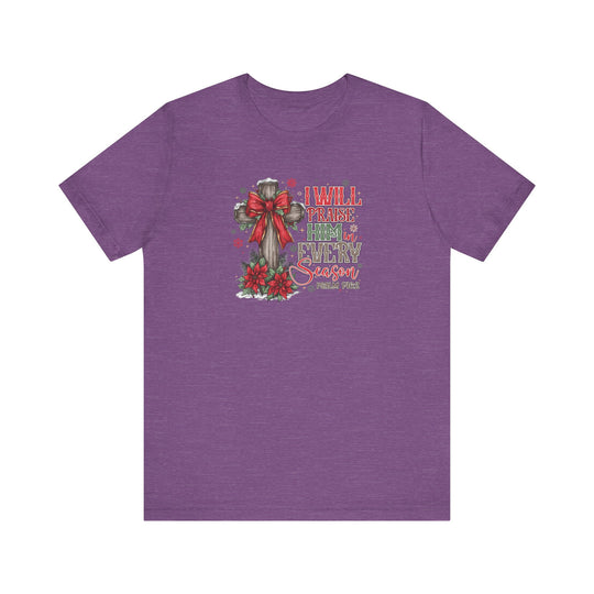 Purple T-shirt featuring a rustic cross with a red bow, poinsettias, and snow-dusted evergreens, captioned I WILL PRAISE HIM in EVERY Season from Faith Family Designs.