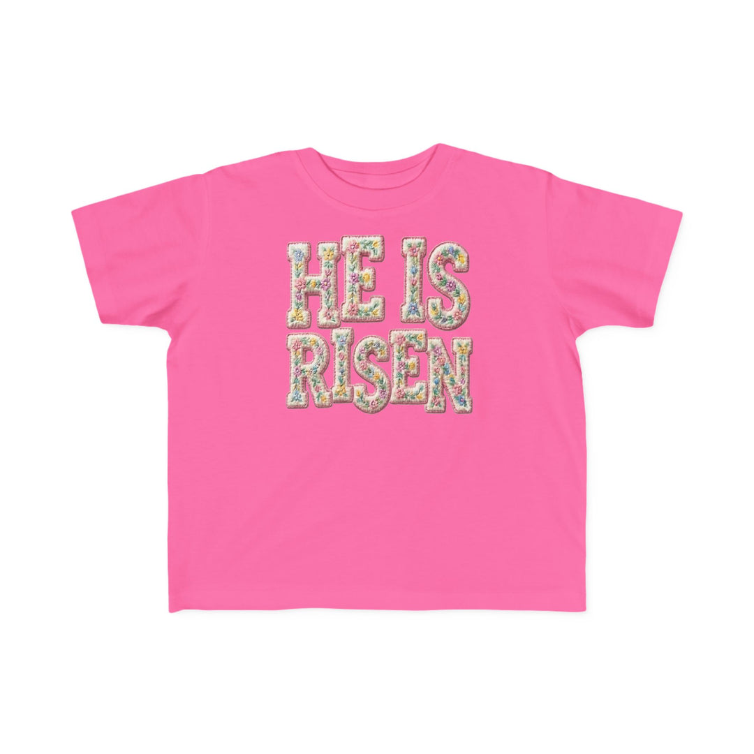 He is Risen Toddler Tee features floral-patterned lettering on a hot-pink T-shirt, designed for comfort and durability, perfect for toddlers.