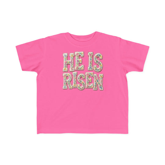He is Risen Toddler Tee features floral-patterned lettering on a hot-pink T-shirt, designed for comfort and durability, perfect for toddlers.