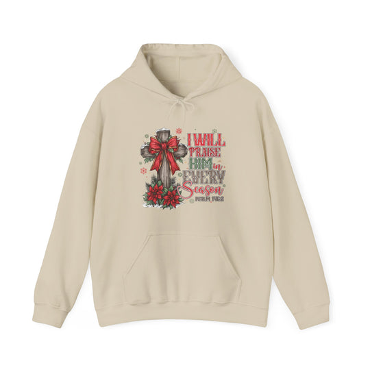 Cream-colored Praise Him in Every Season Hoodie featuring a rustic cross with a red bow, poinsettias, and festive scripture, ideal for cozy, faith-inspired wear.