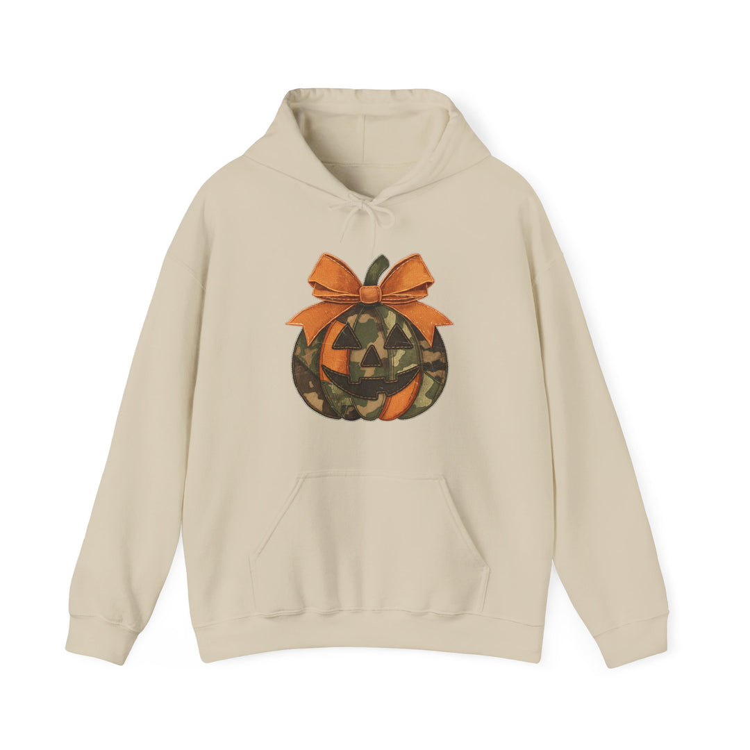 Light-beige hoodie featuring a camouflage and orange jack-o-lantern graphic with a bow, kangaroo pocket, and color-matched drawstring, ideal for cozy, stylish wear.