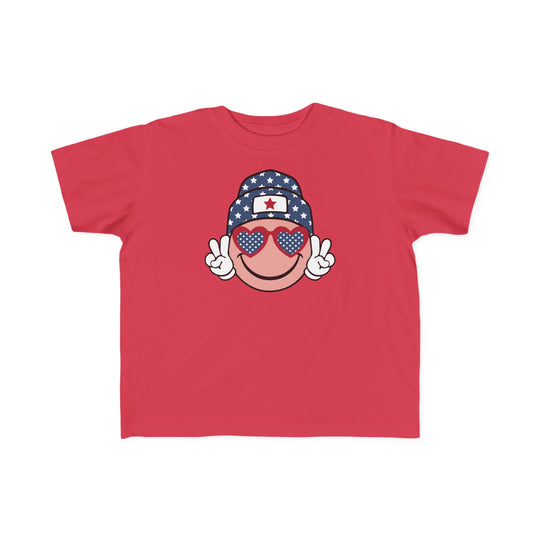 American Girl Toddler Tee featuring a red shirt with a cartoon face, sunglasses, and hat. Soft 100% combed ringspun cotton, light fabric, tear-away label, classic fit. Sizes: 2T, 3T, 4T, 5-6T.