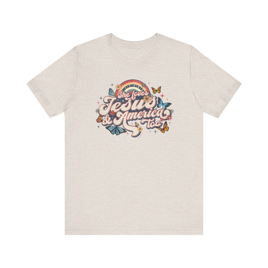 A white t-shirt featuring a graphic design of butterflies and flowers, titled She Loves Jesus and America Tee. Unisex jersey tee with ribbed knit collars, 100% Airlume combed cotton, and tear-away label.