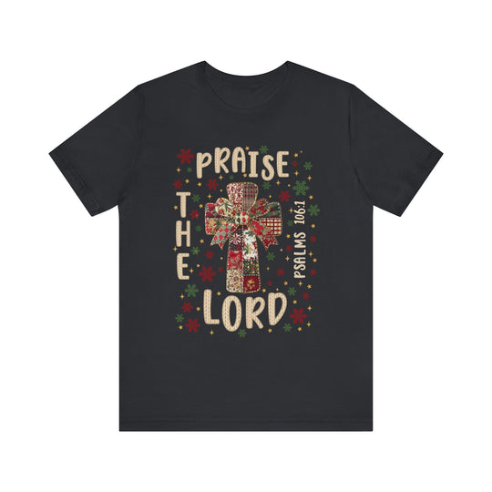 Praise the Lord Tee features a patchwork cross with a bow, surrounded by snowflakes and stars, and includes PSALMS 106:1. Crafted from soft cotton for comfort.