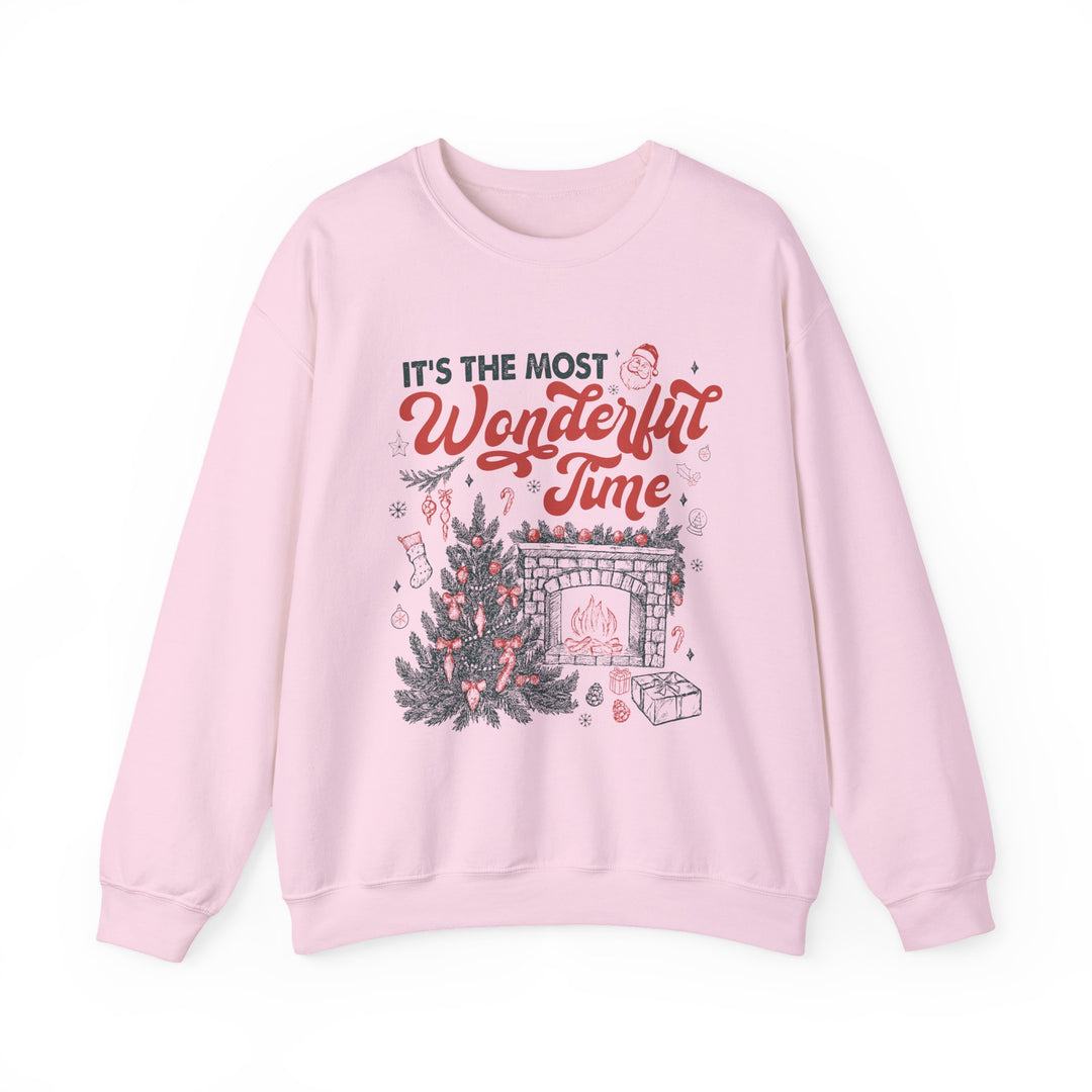Light-pink crewneck sweatshirt featuring It’s the Most Wonderful Time with a festive Christmas tree and fireplace design, embodying cozy holiday spirit.