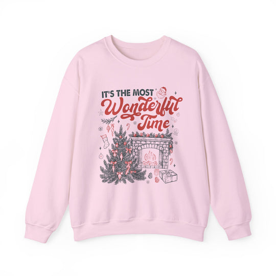 Light-pink crewneck sweatshirt featuring It’s the Most Wonderful Time with a festive Christmas tree and fireplace design, embodying cozy holiday spirit.