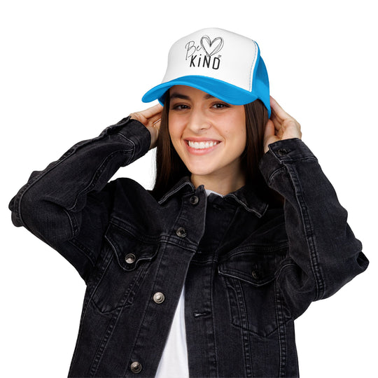 Young woman wearing a Be Kind Foam Trucker Hat, adjusting it with a smile. The hat features a structured, high-profile design with durable, breathable materials.