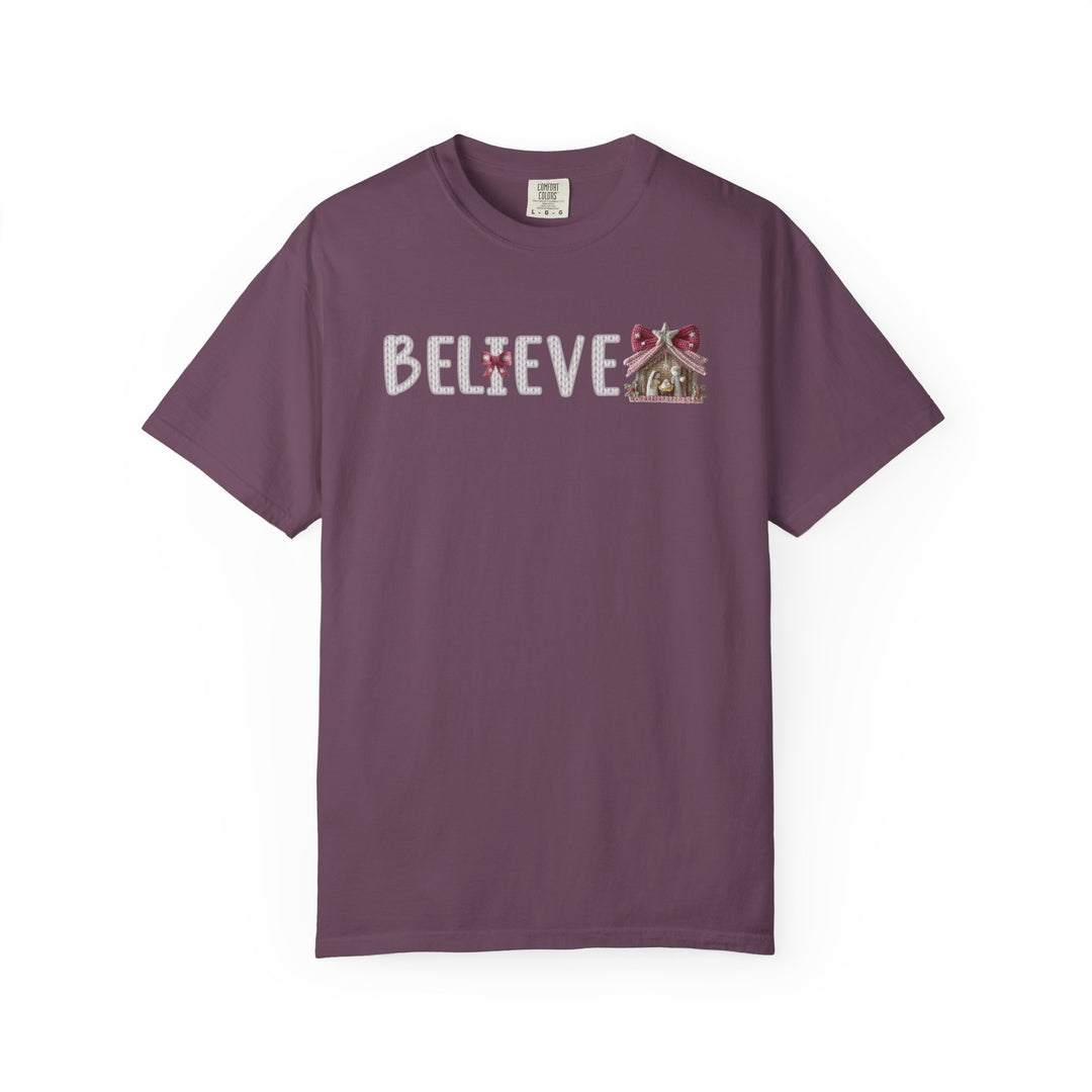 Plum-colored Believe Tee with BELIEVE text, featuring a gingerbread-man as the I and a gingerbread house after E, in a knitted-style font.