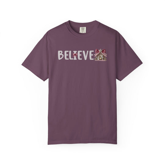 Plum-colored Believe Tee with BELIEVE text, featuring a gingerbread-man as the I and a gingerbread house after E, in a knitted-style font.