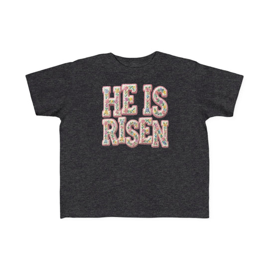 He is Risen Toddler Tee: Dark charcoal-heather oversized tee with HE IS RISEN in pastel floral block letters, designed for toddler comfort and style.
