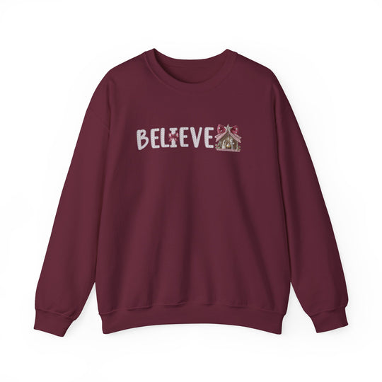 Burgundy crewneck sweatshirt with BELIEVE in stitched letters; gingerbread house motif as the final E. Cozy, unisex design from Faith Family Designs.