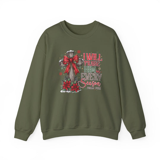 Olive-green sweatshirt features a wooden cross with a red bow, poinsettias, snow, and I will praise Him in every season text from Psalm 146:2.