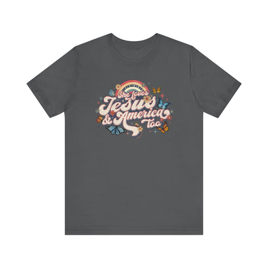 A grey t-shirt featuring a graphic design with butterflies and flowers, titled She Loves Jesus and America Tee. Unisex jersey tee with ribbed knit collars, taping on shoulders, and tear-away label. Made of 100% Airlume combed cotton.