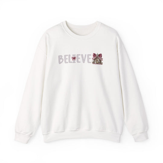 White crewneck sweatshirt with BELIEVE in patterned font, featuring red bows and a gingerbread house, embodying a simple holiday theme.
