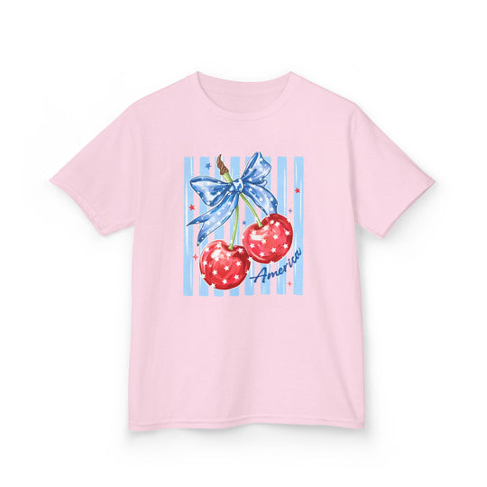 American Cherry Kids Tee featuring red cherries with stars and a blue ribbon on light pink. Durable, soft cotton, perfect for everyday wear.