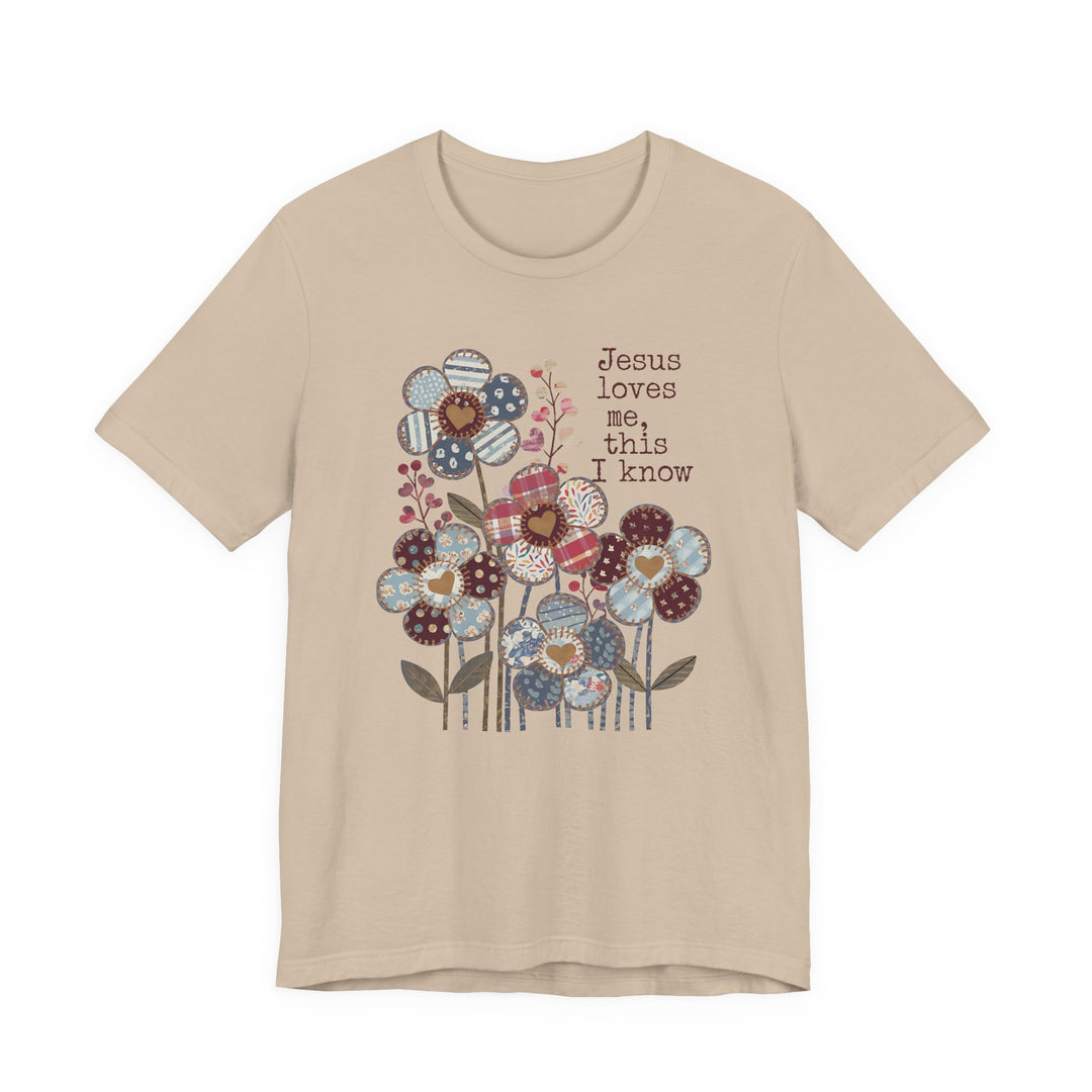 Beige-tan T-shirt with stylized patchwork flowers and Jesus loves me, this I know text in typewriter font, embodying Faith Family Designs' unique graphic style.