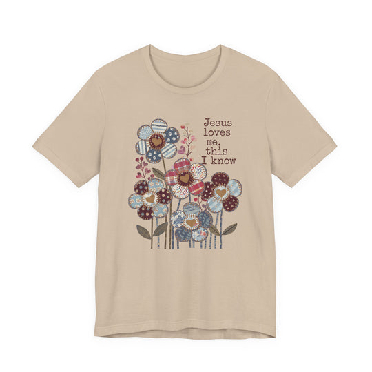 Beige-tan T-shirt with stylized patchwork flowers and Jesus loves me, this I know text in typewriter font, embodying Faith Family Designs' unique graphic style.