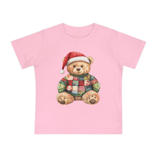 Christmas Bear Baby Tee features a cuddly teddy bear in a Santa hat and patchwork sweater on a light pink T-shirt, perfect for stylish first steps.