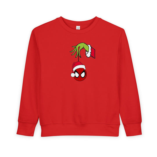 Red toddler crewneck sweatshirt featuring a holiday-themed graphic with the Grinch's hand holding a Spider-Man ornament in a Santa hat.