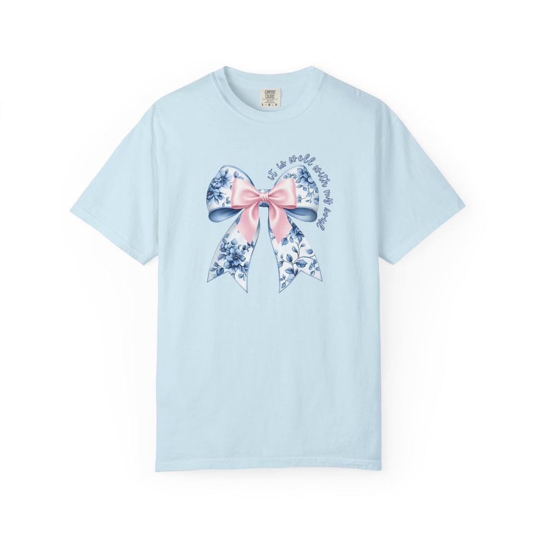 It is Well With My Soul Tee featuring a decorative blue-and-white floral bow with a pink overlay on pale-blue fabric. Comfort Colors label visible.