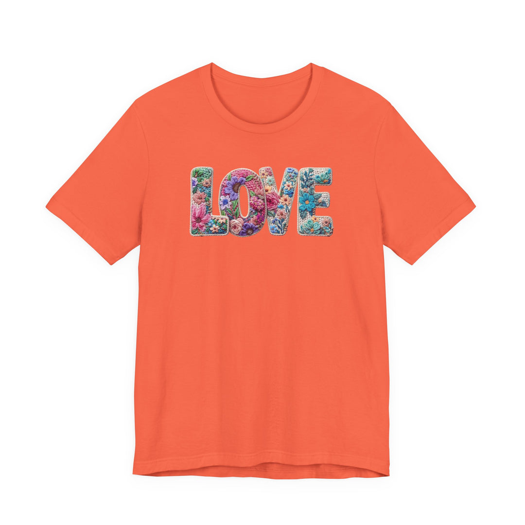 Solid-orange Love Spring Tee featuring LOVE in colorful floral pattern, short sleeves, showcasing soft cotton texture and ribbed knit collar for a comfortable, unisex fit.