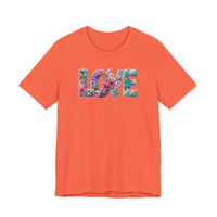 Solid-orange Love Spring Tee featuring LOVE in colorful floral pattern, short sleeves, showcasing soft cotton texture and ribbed knit collar for a comfortable, unisex fit.