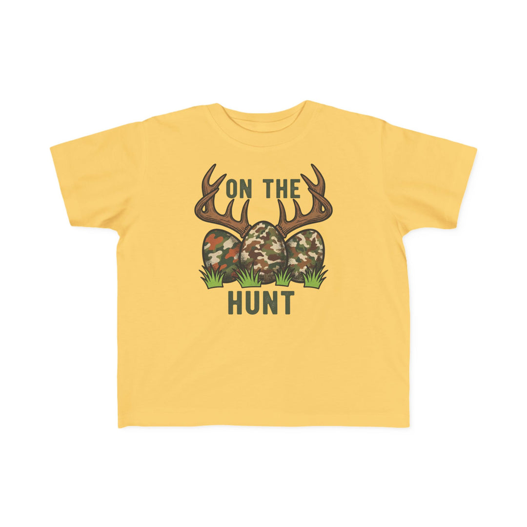 On the Hunt Toddler Tee: Yellow child's T-shirt featuring camouflage eggs with deer antlers and ON THE HUNT text. Soft, durable cotton perfect for toddlers.