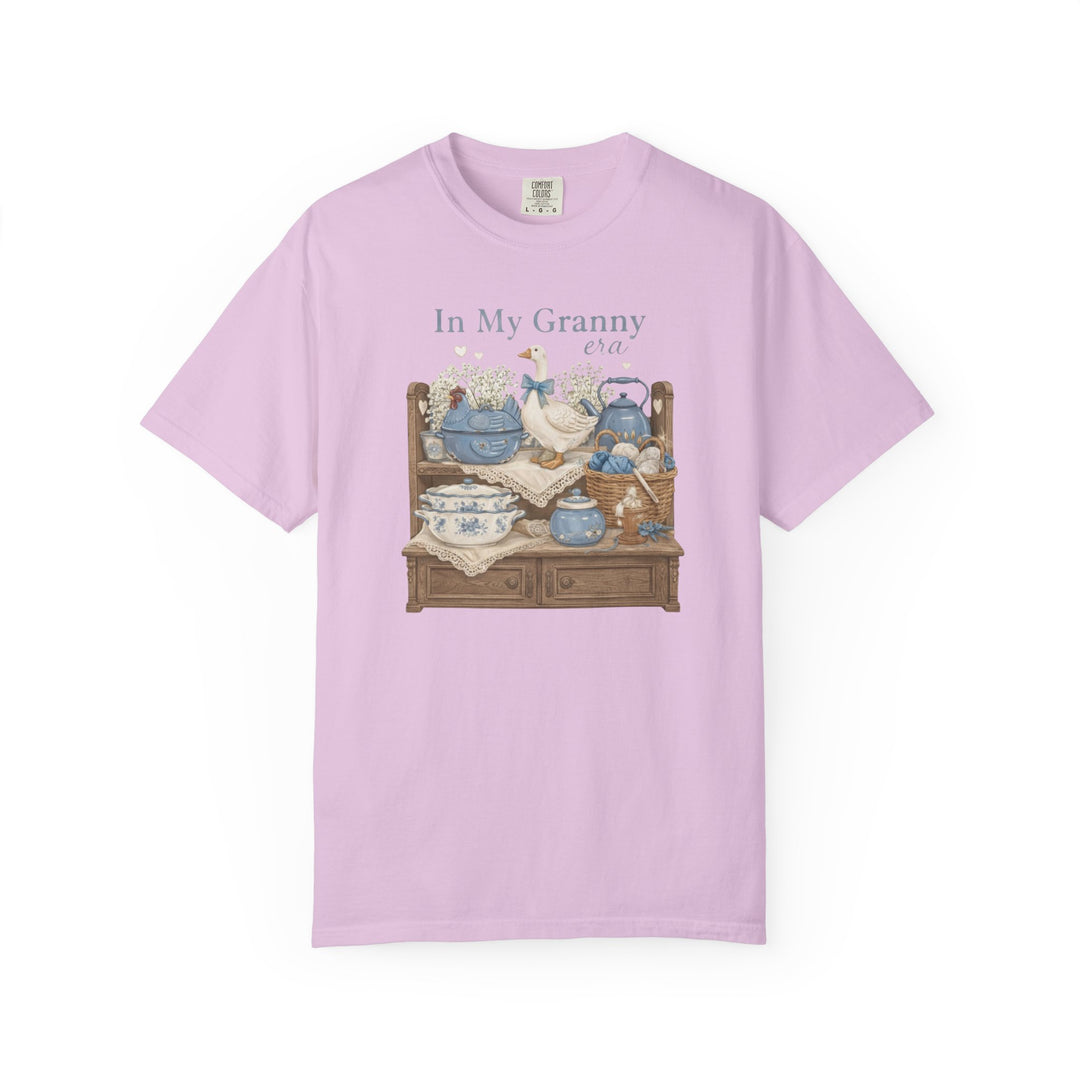 In My Granny Era Tee featuring a charming granny-core still life with a goose, china, yarn, and flowers on a pink short-sleeve T-shirt.