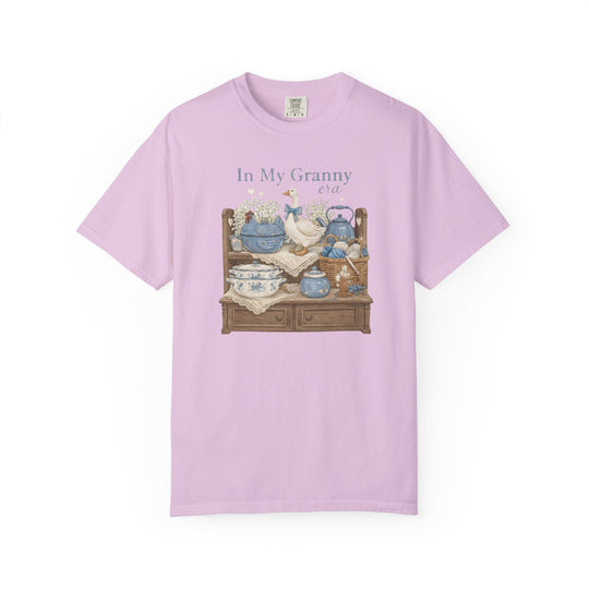 In My Granny Era Tee featuring a charming granny-core still life with a goose, china, yarn, and flowers on a pink short-sleeve T-shirt.