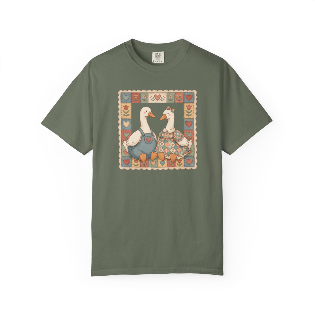 Olive-green Thrifted Geese Tee featuring folk-art-style geese in overalls and dress, framed by hearts and flowers, on Comfort Colors soft, durable cotton.