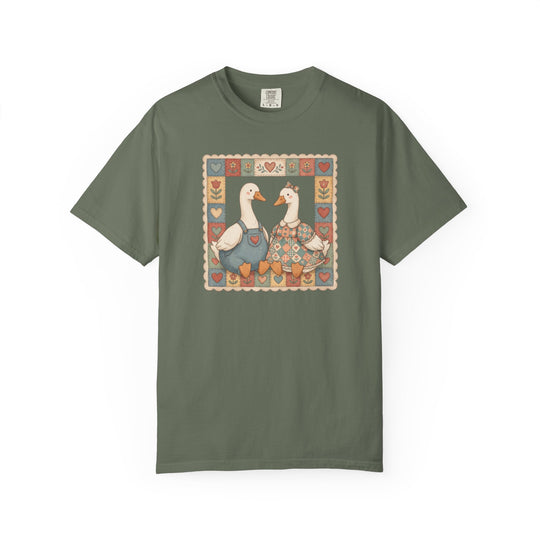Olive-green Thrifted Geese Tee featuring folk-art-style geese in overalls and dress, framed by hearts and flowers, on Comfort Colors soft, durable cotton.